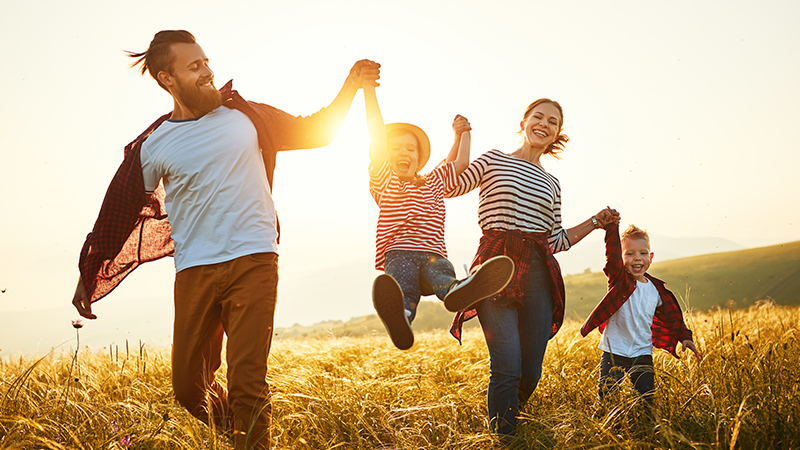 4-köpfige Familie auf Feld mit Sonnenaufgang im Hintergrund.